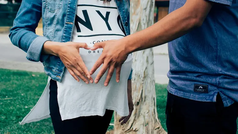 La imagen muestra a una pareja formando un corazón con sus manos sobre el estómago de una mujer embarazada