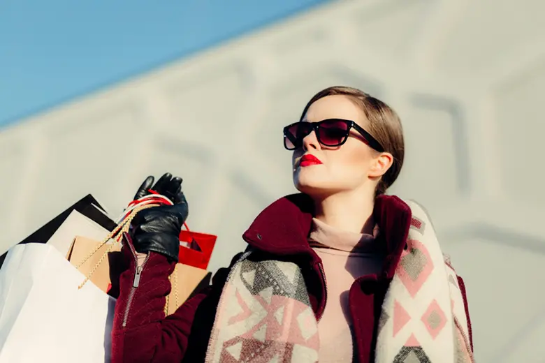 La imagen muestra a una mujer con lentes oscuros cargando varias bolsas tras ir de compras