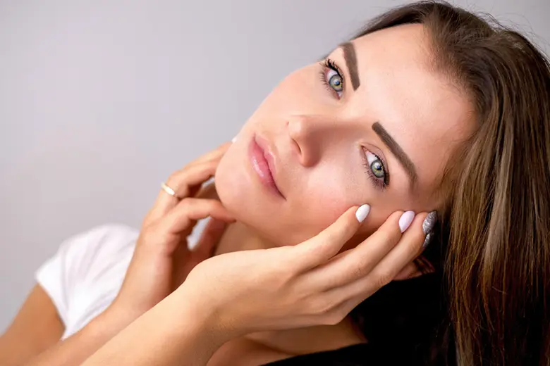 La imagen muestra a una mujer bonita con sus manos alrededor de su rostro