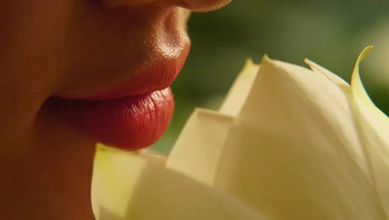 La imagen muestra los labios de una mujer oliendo una flor de loto