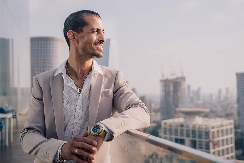 La imagen muestra a un hombre de negocios sonriendo en la terraza de un edificio