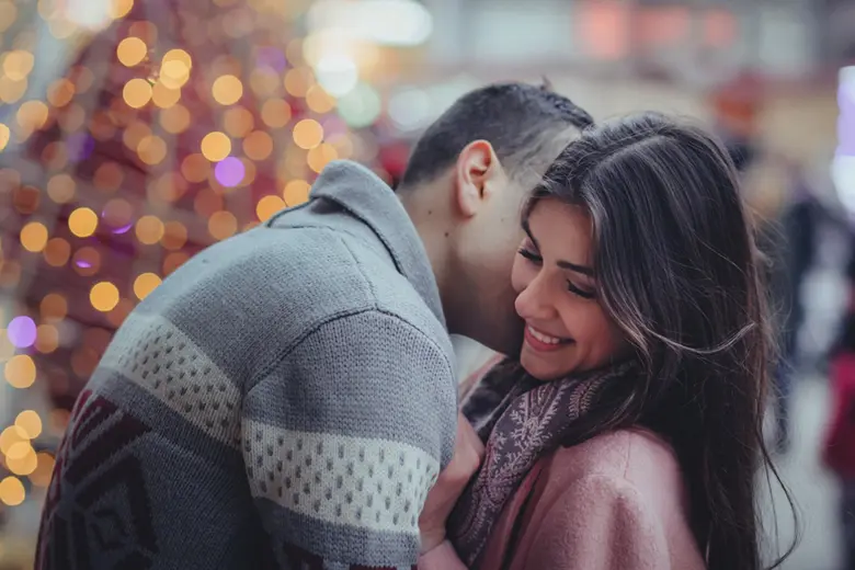 La imagen muestra a una mujer sonriente mientras su pareja le dice algo al oído