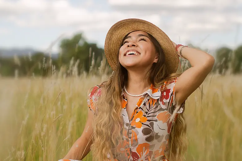 La imagen muestra a una mujer joven sonriente en medio de un campo.